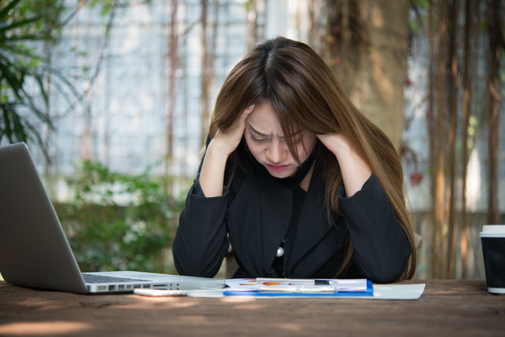 A woman in a business suit stresses over her business debt, sitting in front of a laptop and paperwork.